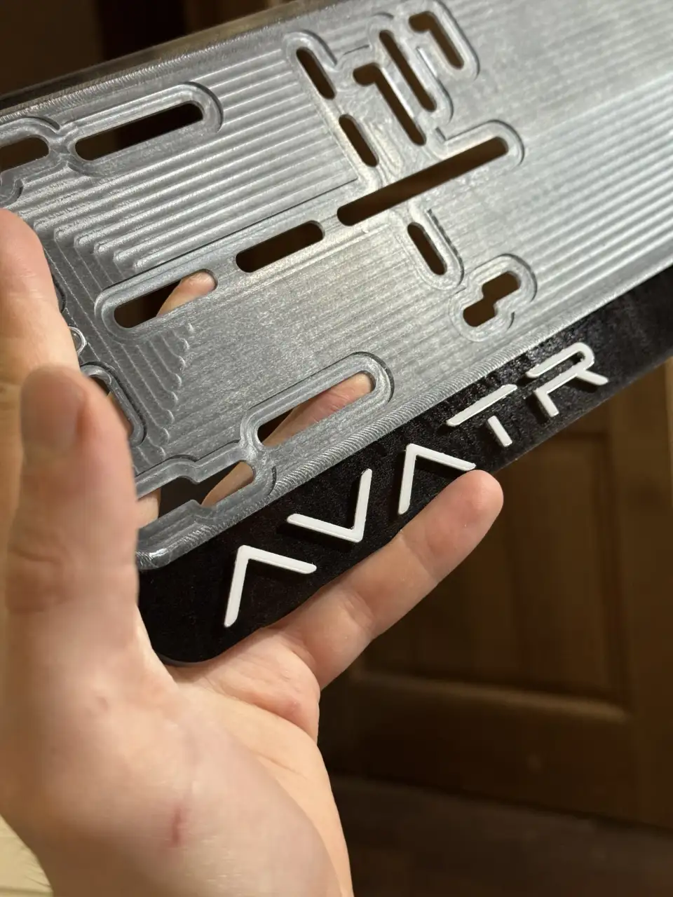 Avatr · логотип крупным планом Макро чёрной номерной рамки Avatr с объёмным белым логотипом