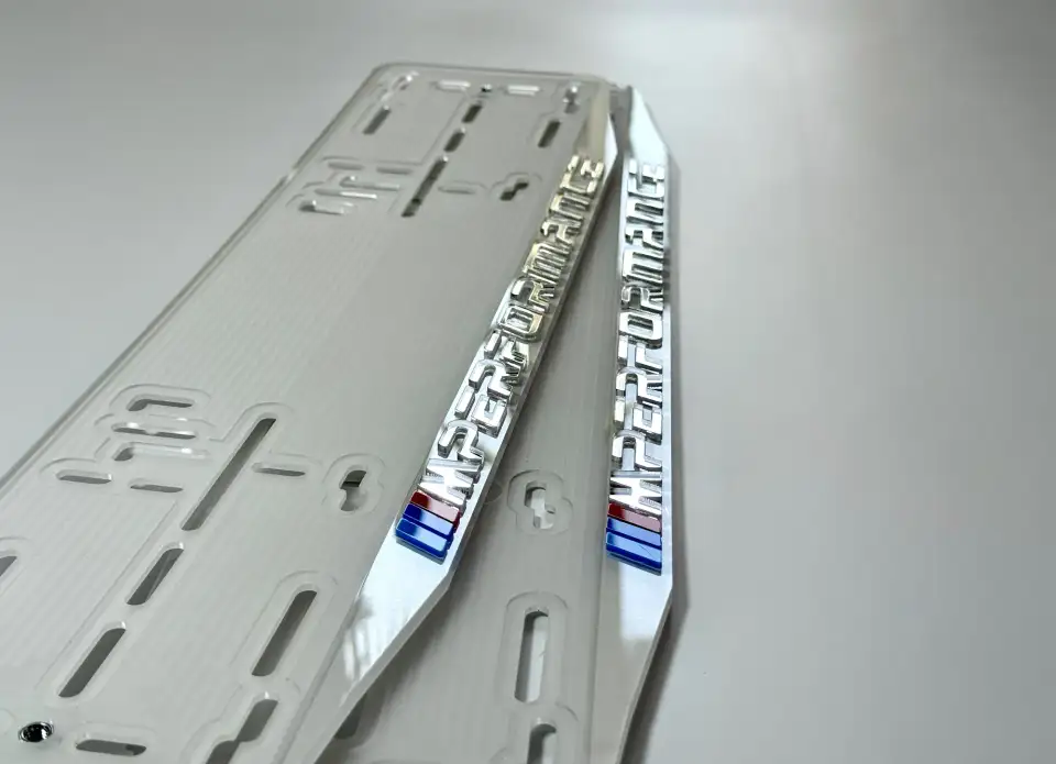 BMW M Performance · крупный план хром-букв Крупный план хромированных букв M Performance с M-полосками на белой номерной рамке BMW