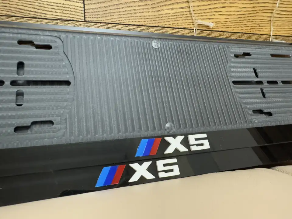BMW X5 · крупный план эмблемы M Крупный план чёрных номерных рамок BMW X5 с эмблемой M и белыми буквами