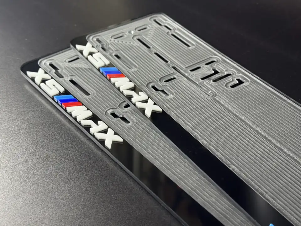 BMW X5 MAX · крупный план шильдика Крупный план шильдика X5 MAX с M-полосками на чёрной номерной рамке