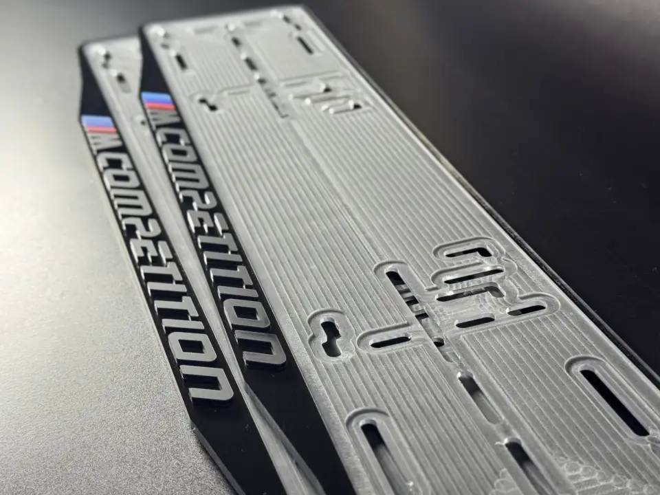 BMW M Competition · крупный план надписи Крупный план надписи M Competition с M-полосками на чёрной номерной рамке