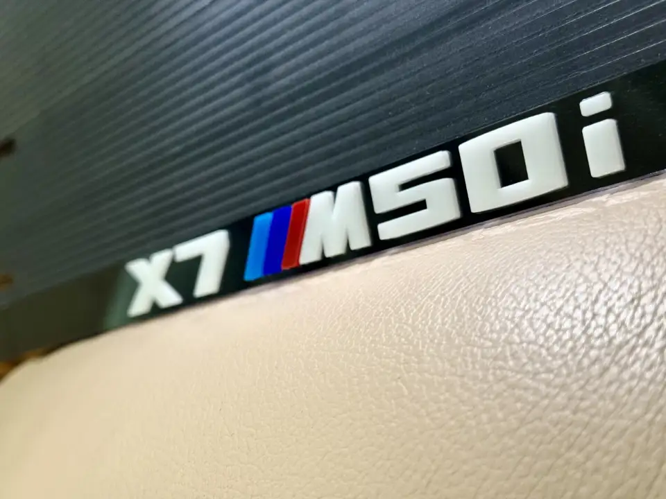 BMW X7 M50i · белые буквы, макро Крупный план надписи BMW X7 M50i на чёрной номерной рамке