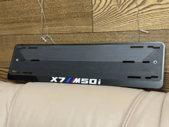 BMW X7 M50i · чёрный глянец, белые буквы Чёрная номерная рамка BMW X7 M50i с белыми буквами и полосками M