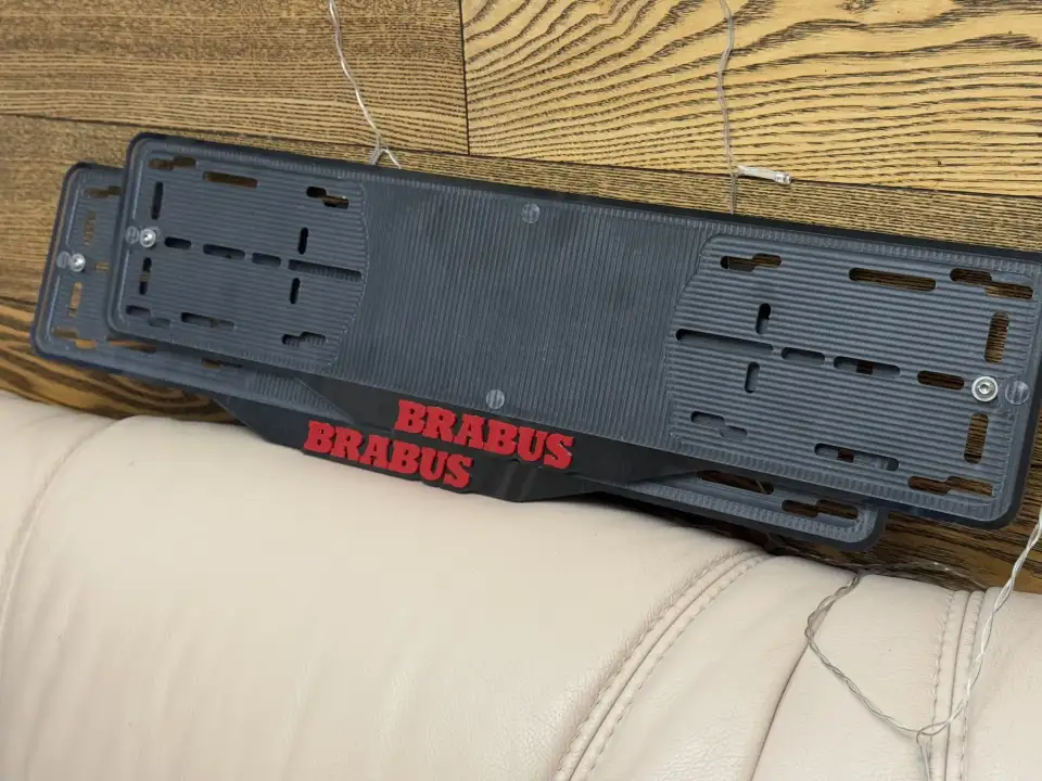 BRABUS · чёрные рамки, красные буквы Две чёрные номерные рамки BRABUS с красными буквами на деревянной стене