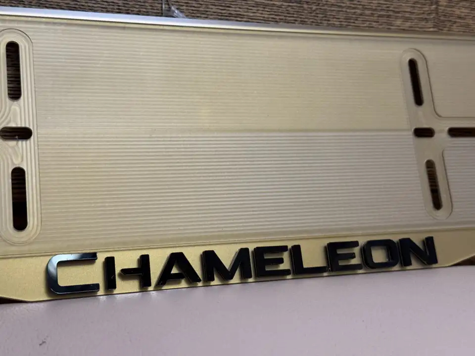 CHAMELEON · макро чёрных хром-букв на золоте Макро золотистой номерной рамки CHAMELEON с чёрными хромированными буквами
