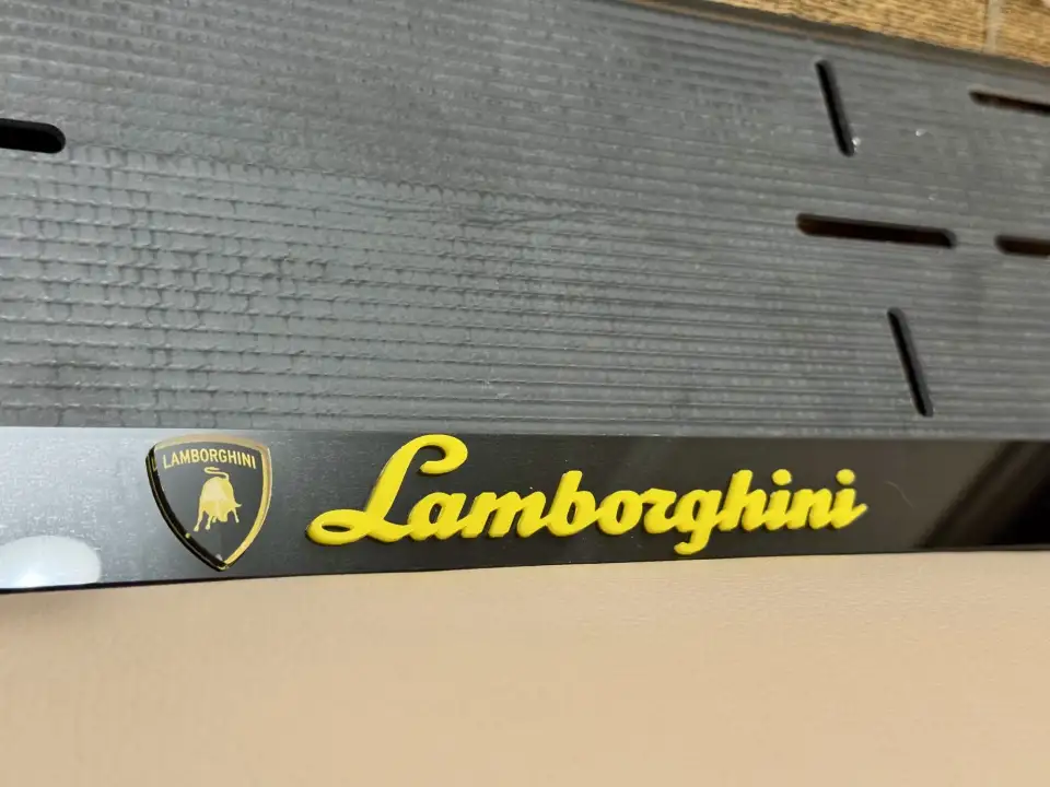 Lamborghini · жёлтые объёмные буквы, крупный план Крупный план жёлтой надписи Lamborghini с золотым щитком на чёрной номерной рамке
