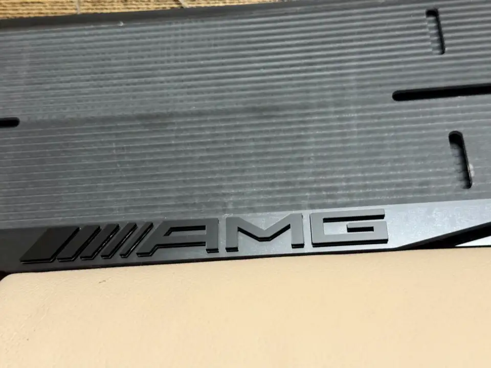 Mercedes-AMG · чёрные буквы на чёрном, макро Крупный план глянцевой чёрной надписи AMG на чёрной номерной рамке