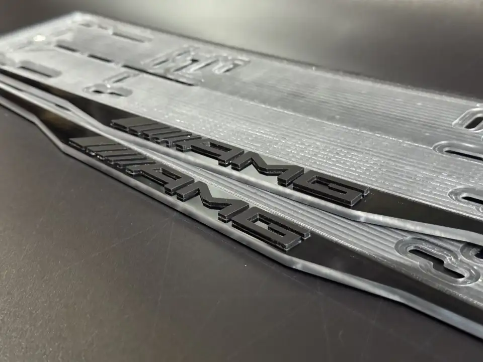 Mercedes-AMG · чёрные глянцевые буквы, макро Макросъёмка глянцевых чёрных букв AMG на номерной рамке Mercedes-AMG