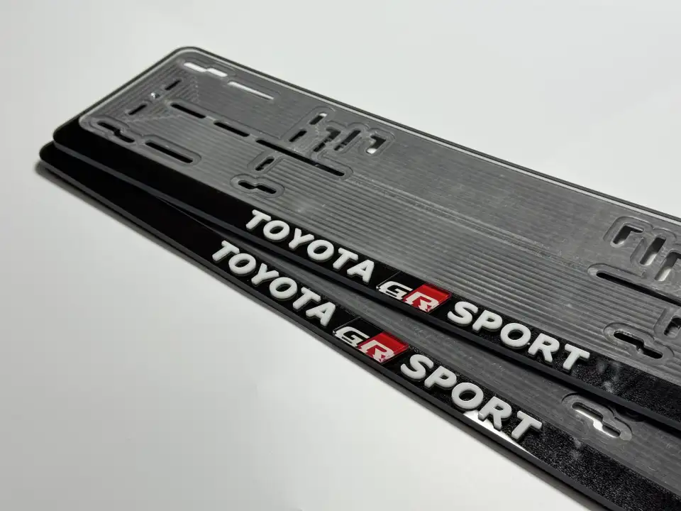 Toyota GR Sport · надпись крупным планом Крупный план чёрной номерной рамки Toyota GR Sport с белыми объёмными буквами