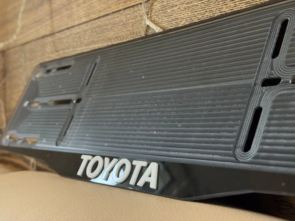 Toyota · крупный план букв Крупный план чёрной номерной рамки Toyota с объёмными буквами
