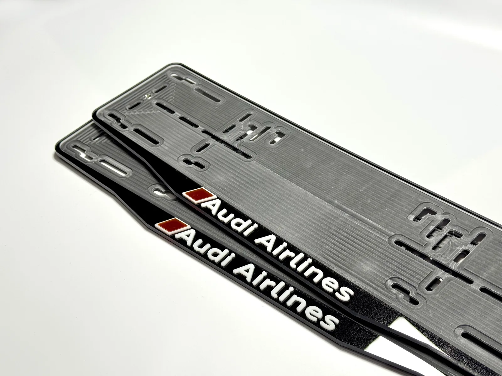 Две чёрные номерные рамки с белыми объёмными буквами Audi Airlines и красным знаком-параллелограммом