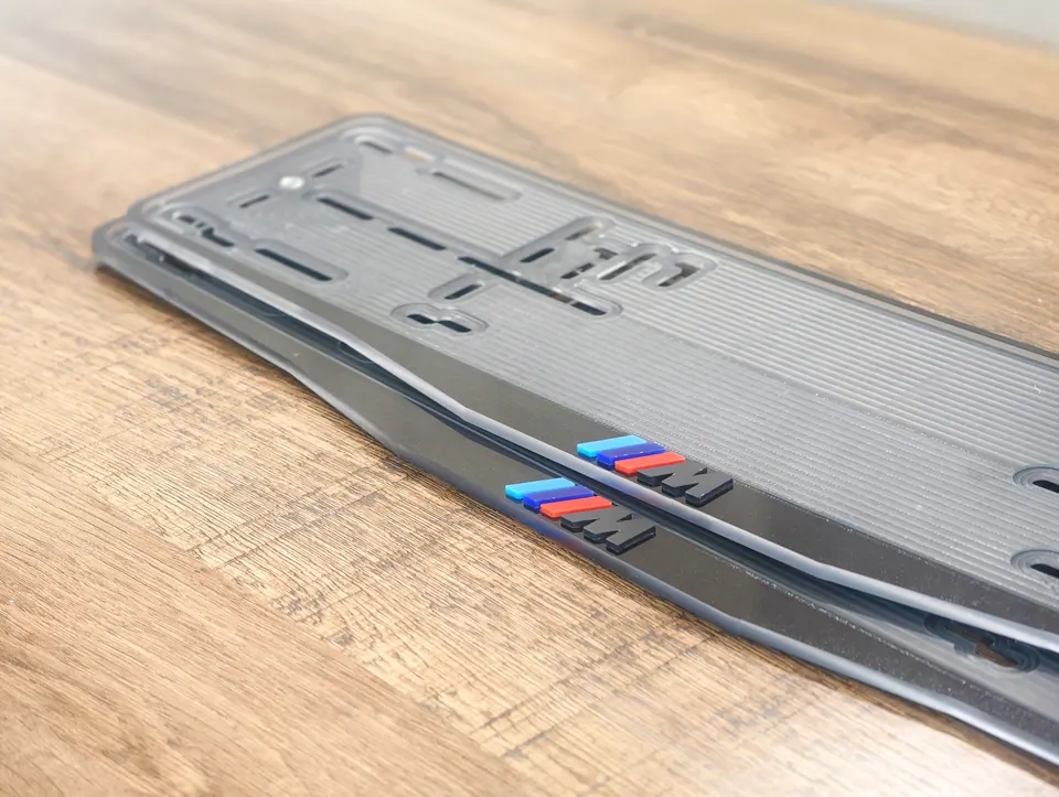 «M» · BMW · чёрный глянец, разноцветные буквы Номерная рамка BMW с надписью «M», цвет рамки - чёрный глянец, разноцветные объёмные буквы, другой ракурс